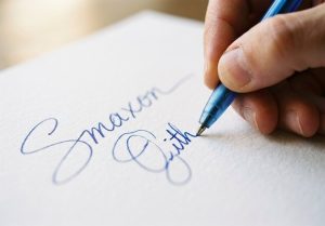 Рука ставит подпись синей ручкой на бумаге