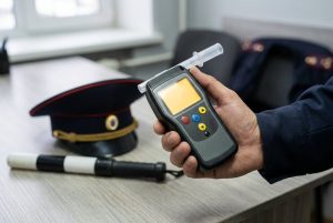 Алкотестер в руке на фоне фуражки и жезла